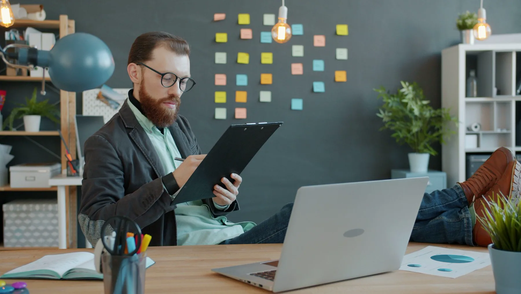 A small business owner writing notes beside a laptop