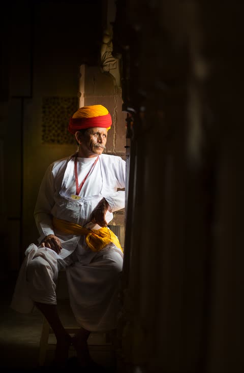 A seated figure in white clothing framed by a wooden doorway