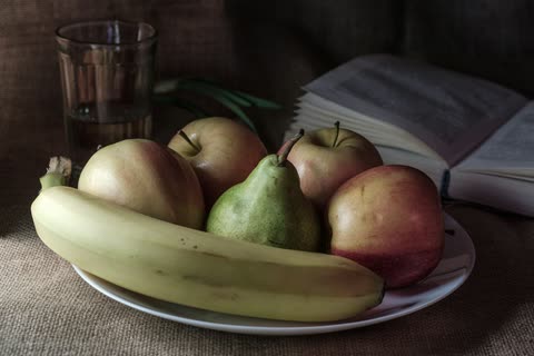 Fruit arranged beside an open book and a glass of water